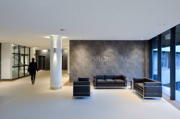 Moderne entreehal van Ypsilon Park met zwarte leren zitbanken en een wand met naamlogo.
